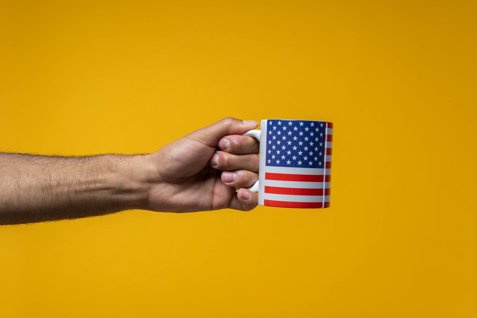 A hand holds a mug featuring the American flag against a bright yellow background.